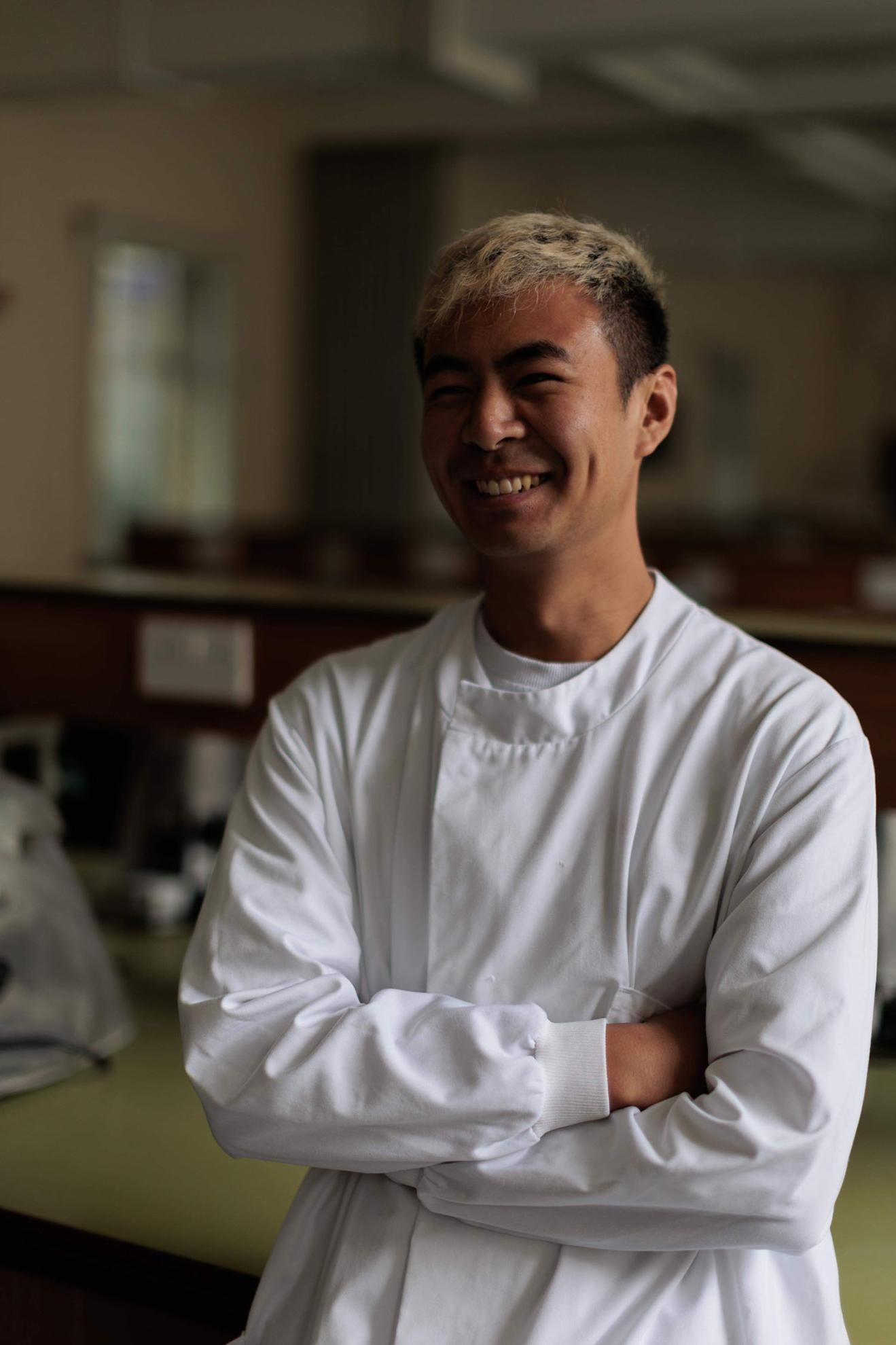 Apprentice Chris in white lab coat with arms folded