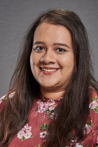 Nazia Thakur in a red top with pink flowers, in front of a grey backdrop