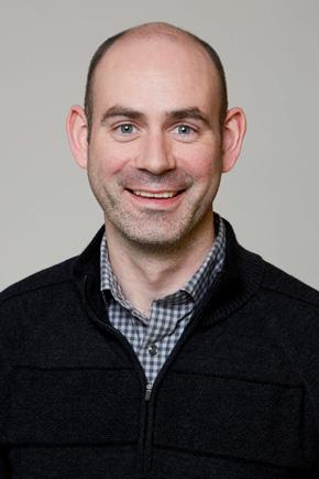 Dr Trevor Sweeney, smiling. Head and shoulders image of Trevor in a grey checked shirt with a black jumper over it.