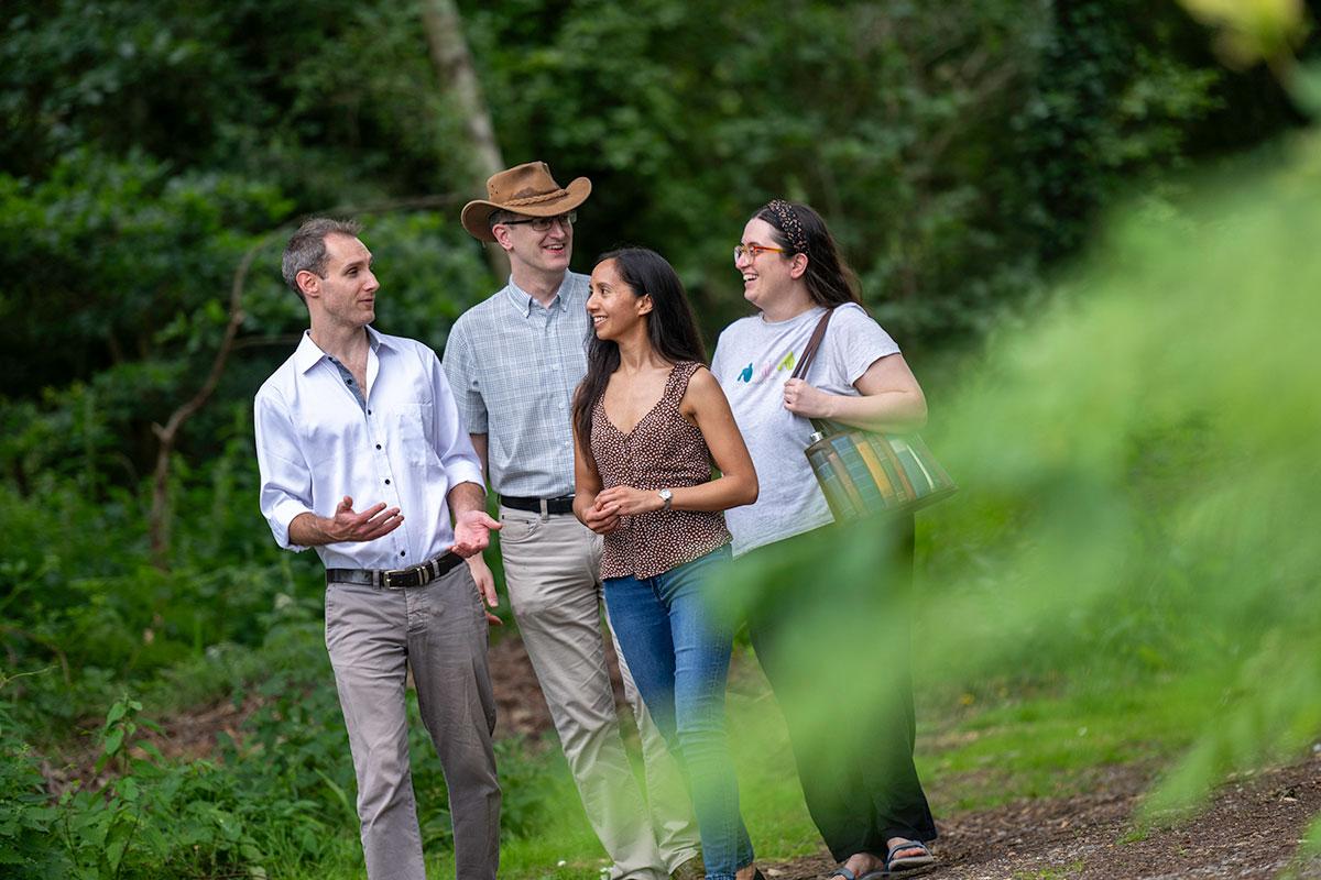 Group of four smiling people conversing while walking through wooded area