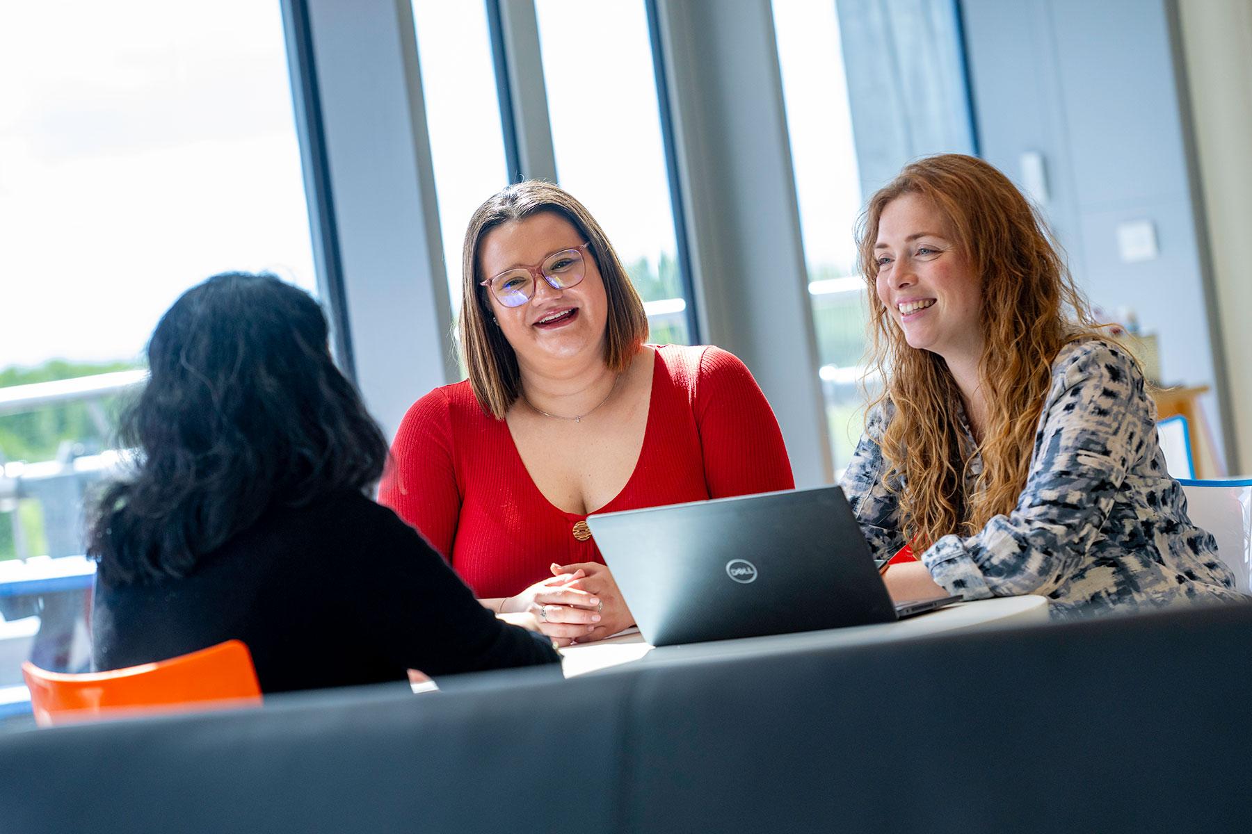 Three happy people sat at a table with a laptop