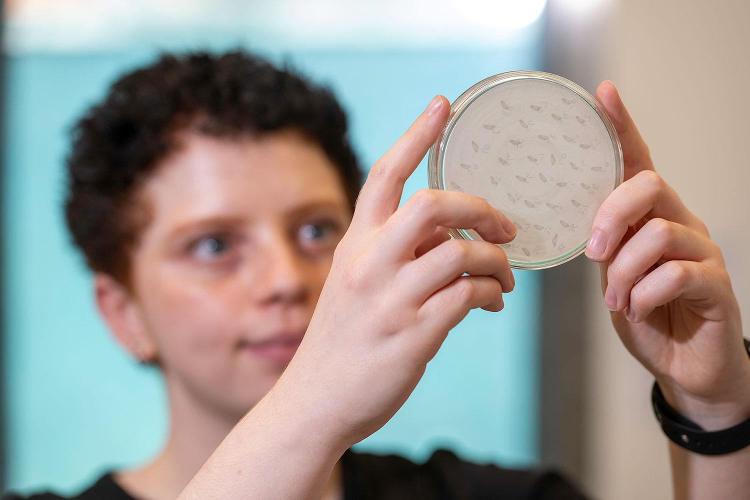 Person holding a petri dish looking up