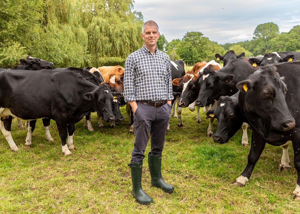 Man stood on grass wearing wellies surrounded by cows