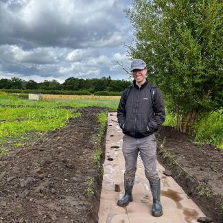 Jim Chadwick in wellies stood on long section of ground covered in brown paper. Behind him is a green field and trees in the distance