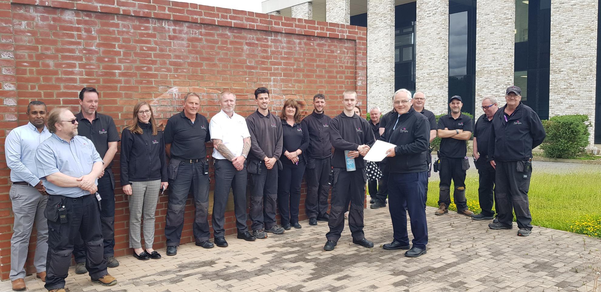 Members of the Estates and Engineering teams stood in front of brick Bull with presentation of certificate to one member