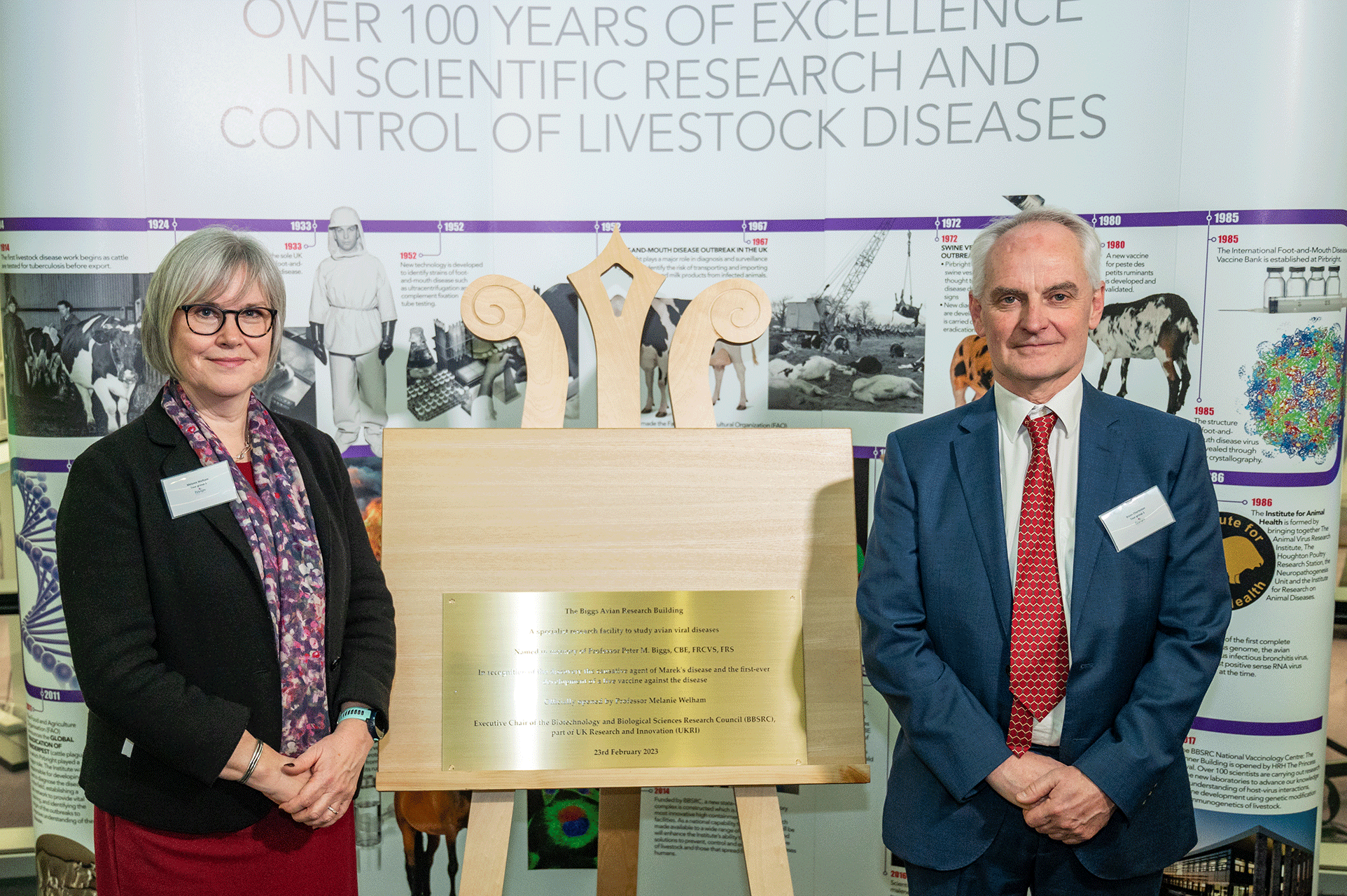 Melanie Welham and Bryan Charleston stood either side of an easel stand which holds a brass plaque