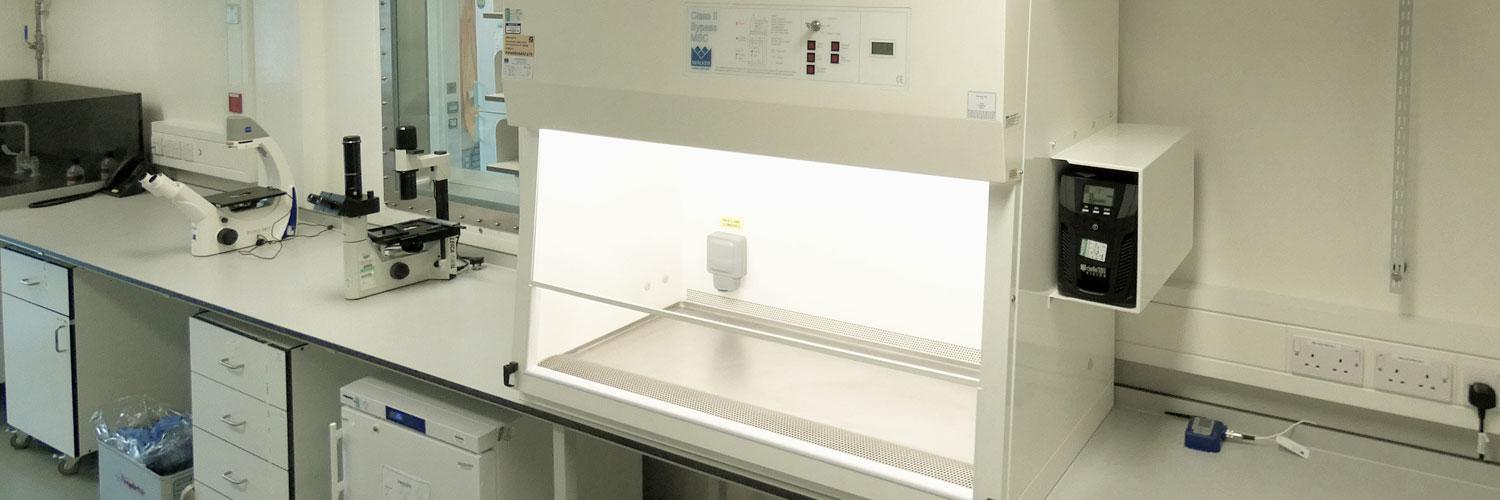 Biological safety cabinet, lights on, next to two microscopes in a Pirbright laboratory