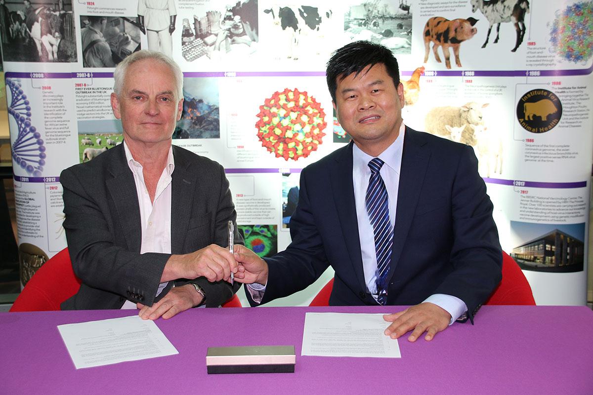 Bryan Charleston and Zheng Haixue at a purple table holding a pen with papers in front of them