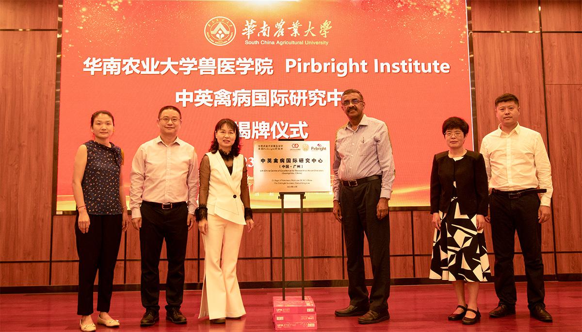 Six people stood around a plaque in front of a screen with a red backgroun containing text that reads Pirbright Institute and Chinese text. Pirbright's Venu Nair and Yongxiu Yao stood in the middle to the right of the plaque.