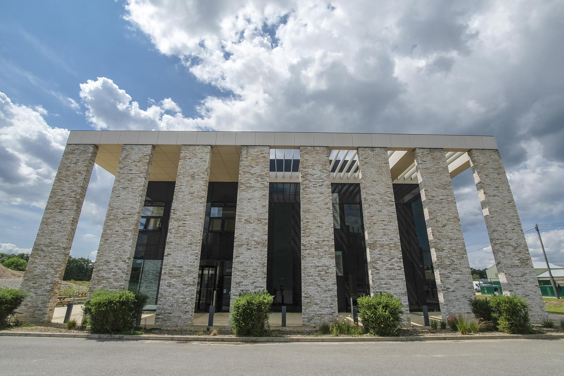 Photo of the front exterior of Pirbright's Jenner building. There are eight stone pillars. Blue sky with fluffy white clouds are see