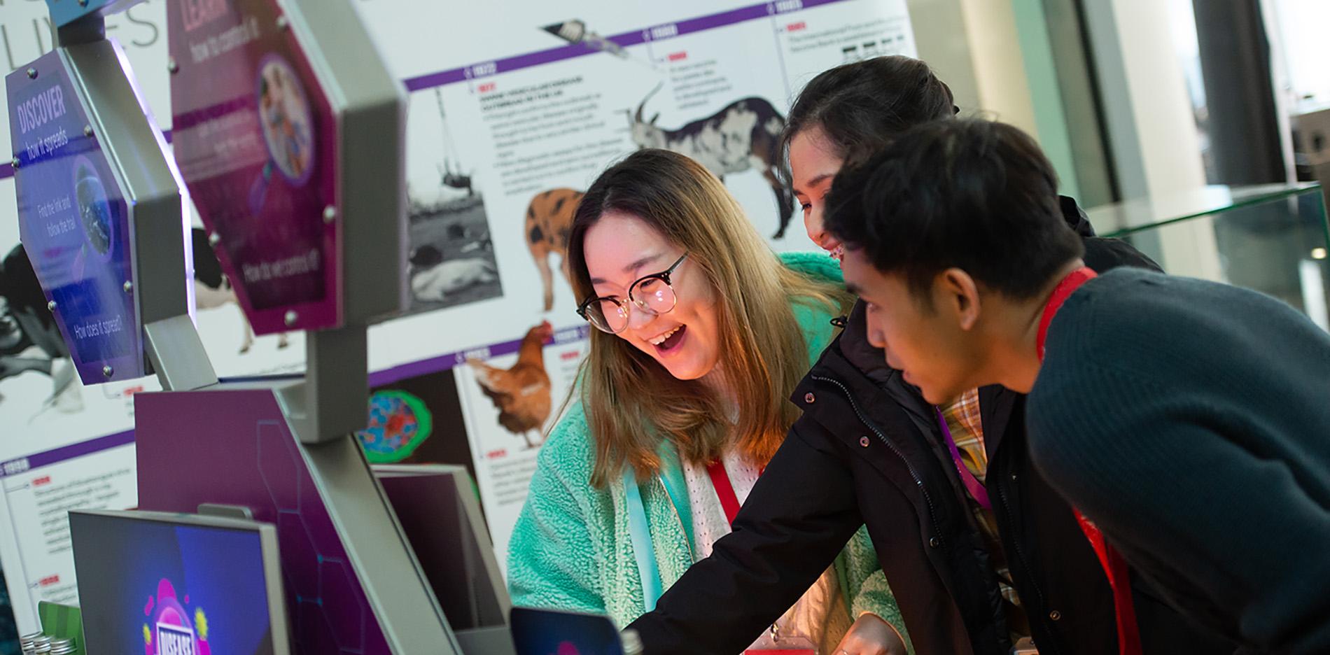 Three young visitors engaging with a screen. One is smiling and another is inquisitive